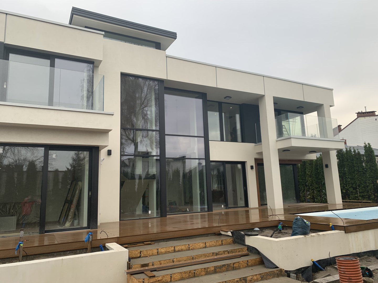 Nowoczesna willa z ogromnymi szklanymi fasadami i tarasem w trakcie prac wykończeniowych – przykład wysokiego standardu budowy.