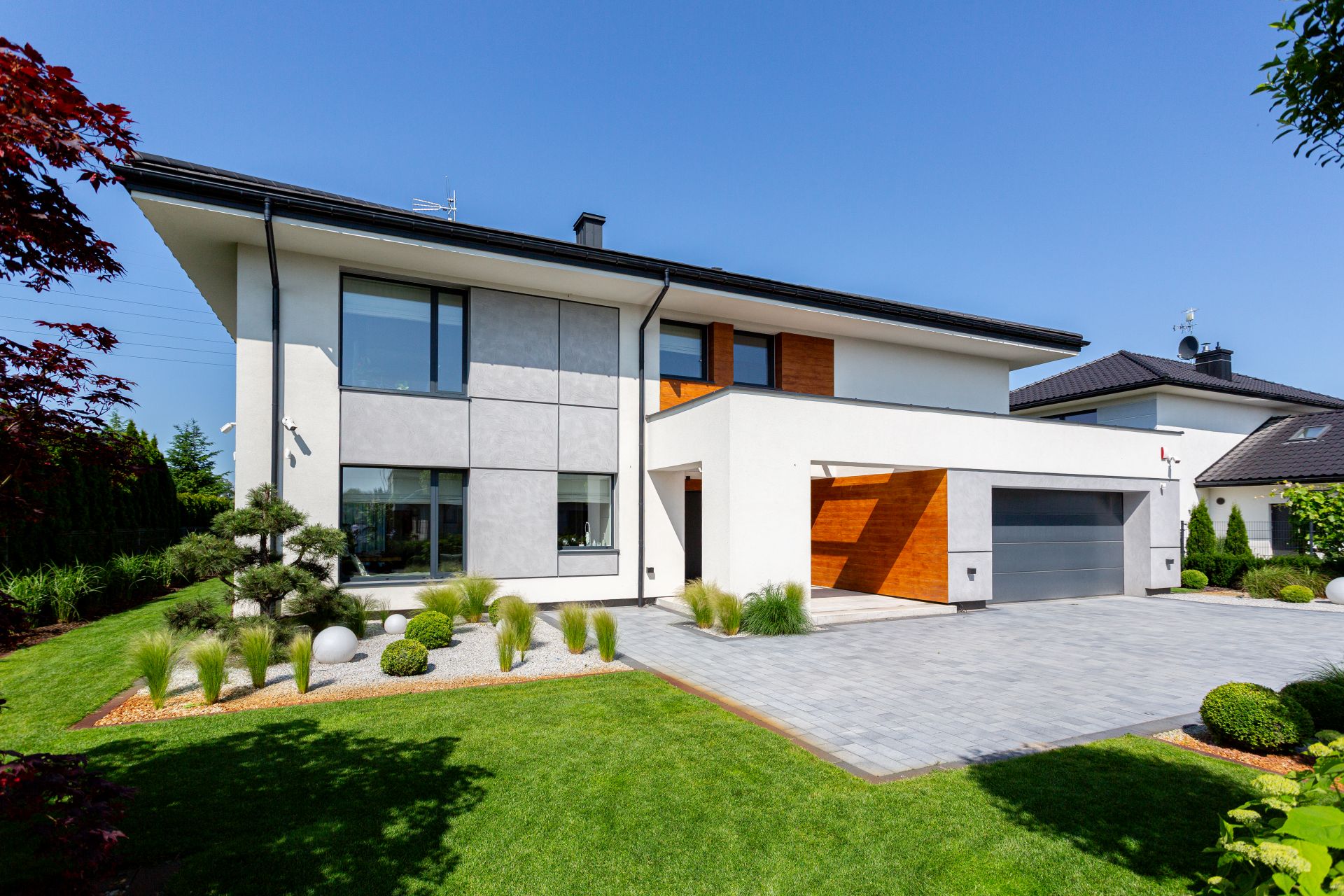 Nowoczesny dom jednorodzinny z wykończoną elewacją i dużym podjazdem z kostki brukowej, ilustrujący niedoszacowane wydatki na zagospodarowanie terenu wokół budynku.