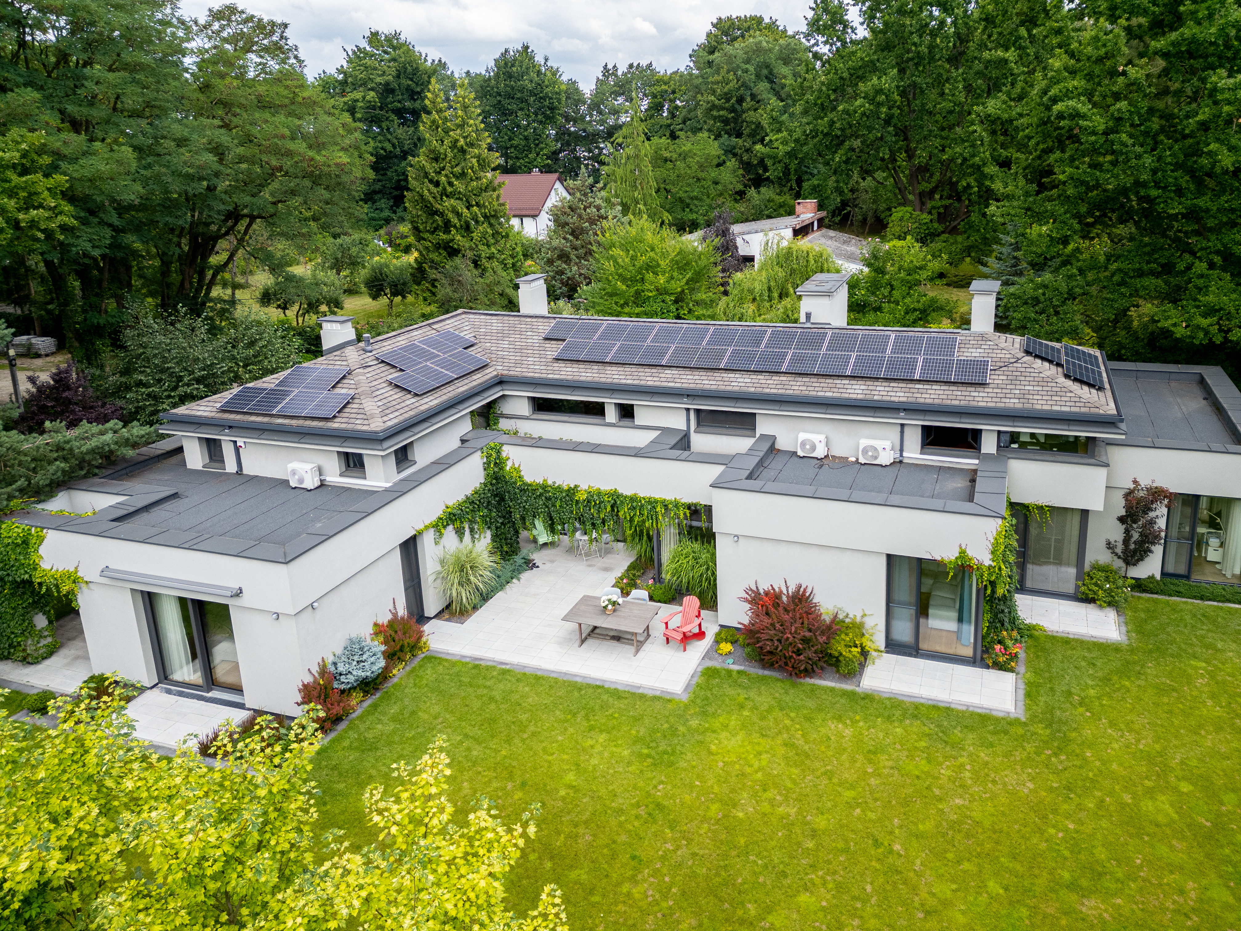 Widok z drona na nowoczesny dom jednorodzinny New-House z panelami słonecznymi na dachu, wewnętrznym patio i zaaranżowanym ogrodem.