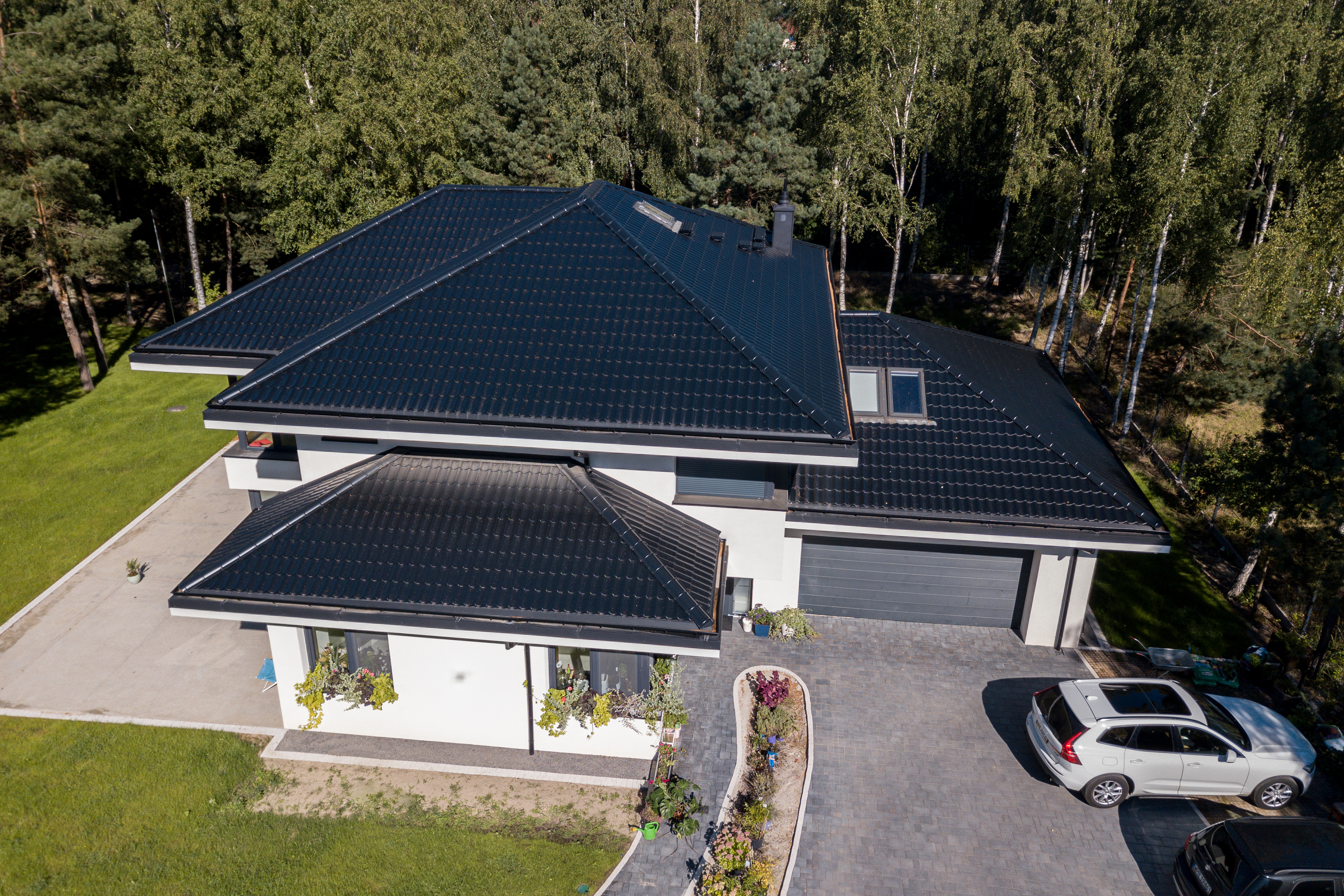 Nowoczesny dom jednorodzinny z czarnym dachem wielospadowym, wybudowany przez firmę New-House. Widok z lotu ptaka przedstawia gotową inwestycję "pod klucz", która jest bezpieczną alternatywą dla zmian w przepisach planistycznych w 2026 roku.