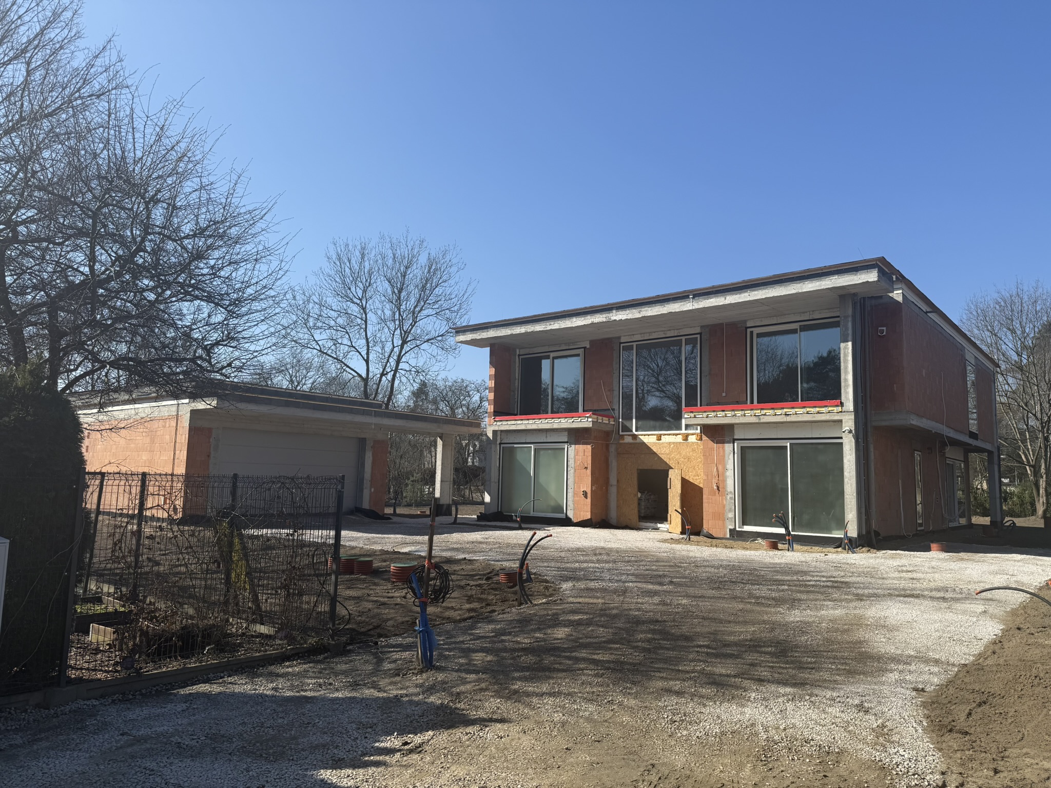 Budynek w stanie surowym zamkniętym realizowany przez firmę New-House. Widoczna solidna konstrukcja z cegły ceramicznej, betonowe podciągi oraz profesjonalnie przygotowane zaplecze budowy.