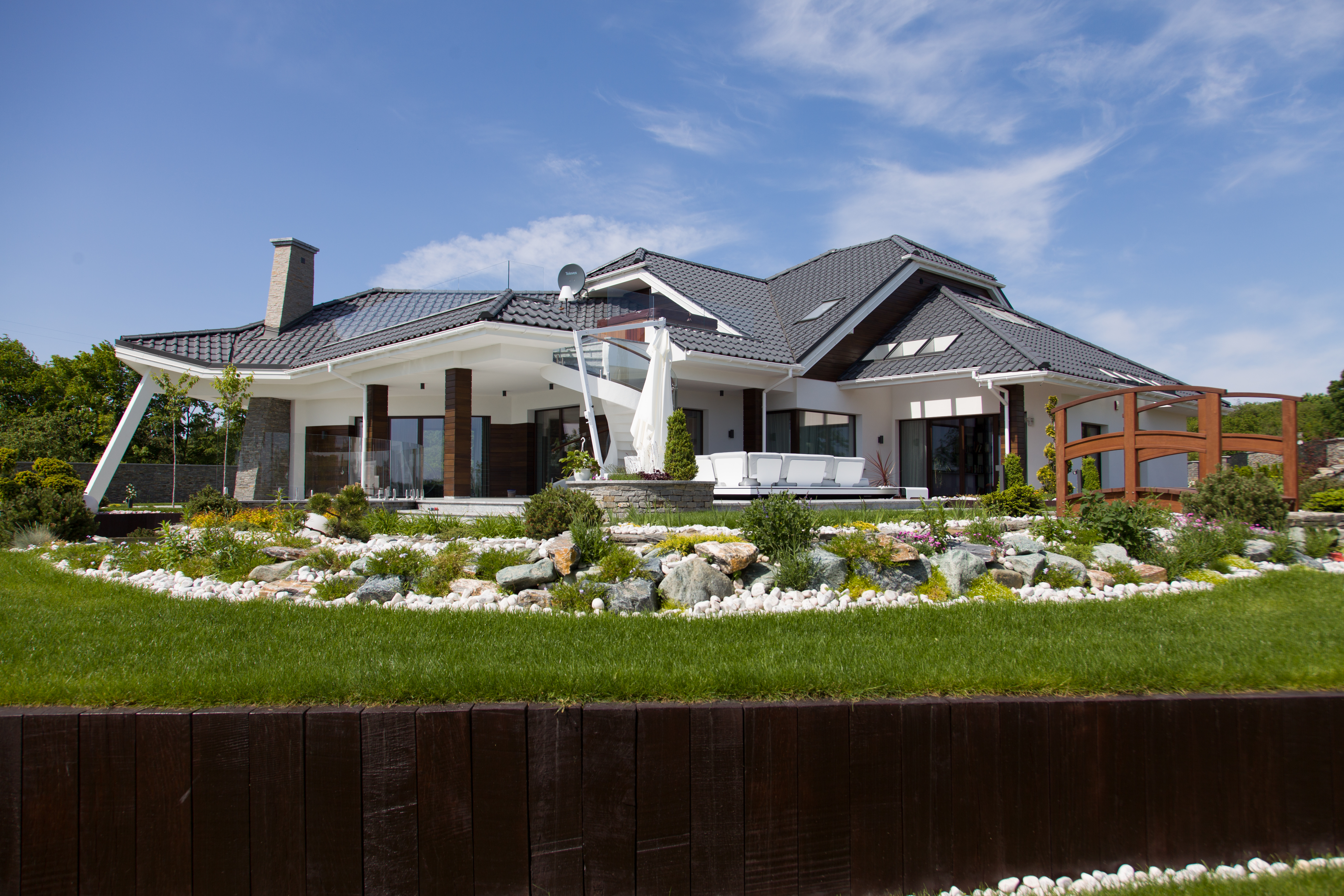 Luksusowa posiadłość z drewnianą elewacją i ozdobnym mostkiem w ogrodzie – realizacja projektu indywidualnego New-House.